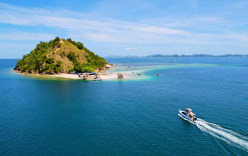 Aerial view of Kelor Island with white sandy beach, turquoise water, and green hill near Labuan Bajo, Indonesia.
