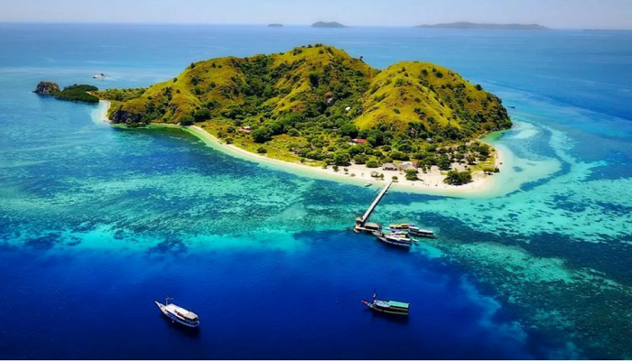 Aerial view of Kelor Island with white sandy beach, turquoise water, and green hill near Labuan Bajo, Indonesia.