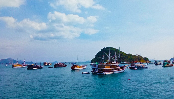 Traveler trekking Kelor Island hill with turquoise sea and white sand, a must-visit stop on Komodo tour packages from Lombok or Bali.