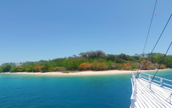 Aerial view of Bidadari Island near Labuan Bajo with turquoise waters, white sand beach, and lush green forest.