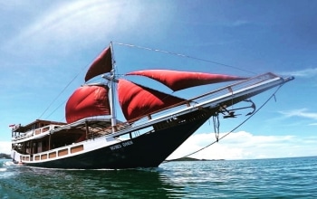 Traditional Phinisi boat sailing near Komodo National Park with clear water and island hills