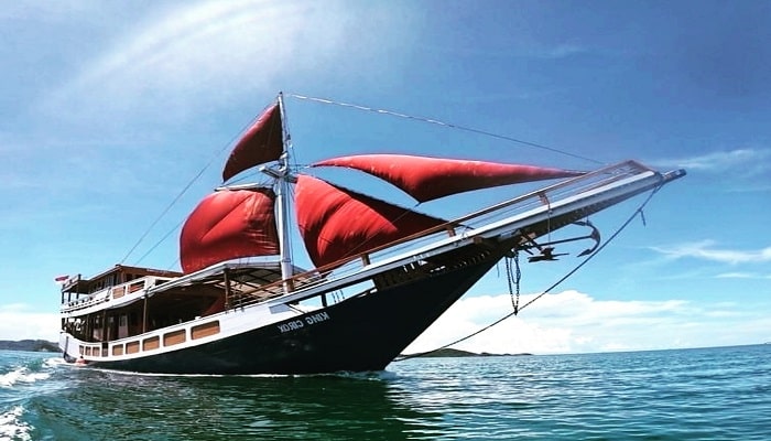 Traditional Phinisi boat sailing near Komodo National Park with clear water and island hills
