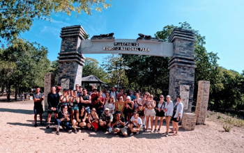 Colorful traditional Bugis-style fishing boats (perahu) docked near the Komodo Village pier, with women drying seaweed or mending nets in the sun