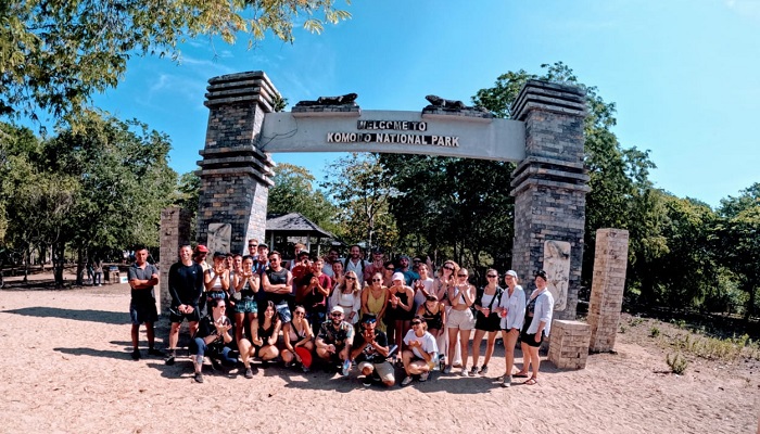 Colorful traditional Bugis-style fishing boats (perahu) docked near the Komodo Village pier, with women drying seaweed or mending nets in the sun