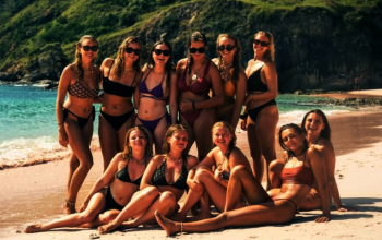 Panoramic view of Komodo Village stilt houses (rumah panggung) over the water with rugged, dry hills in the background, near a Komodo boat trip dock.