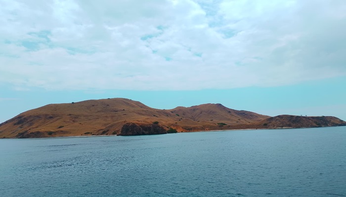 Luxury boat sailing between Komodo Islands during sunset, surrounded by turquoise waters and golden skies.
